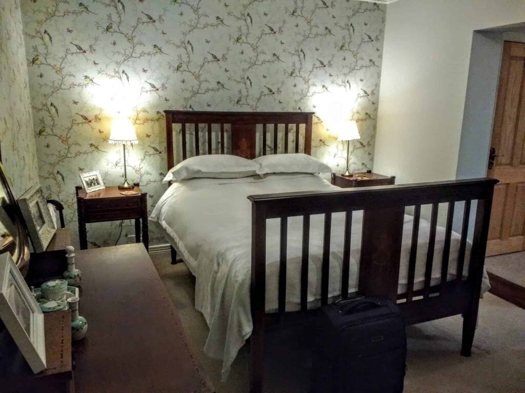 A tidy bedroom with a Carrick-a-Rede rope bridge-themed wooden bed frame, matching bedside tables with lamps, and patterned wallpaper.