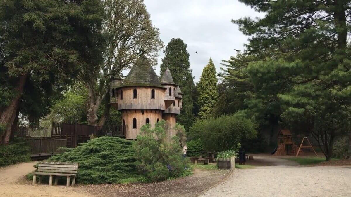 Wooden castle-like structure surrounded by trees in a park setting.