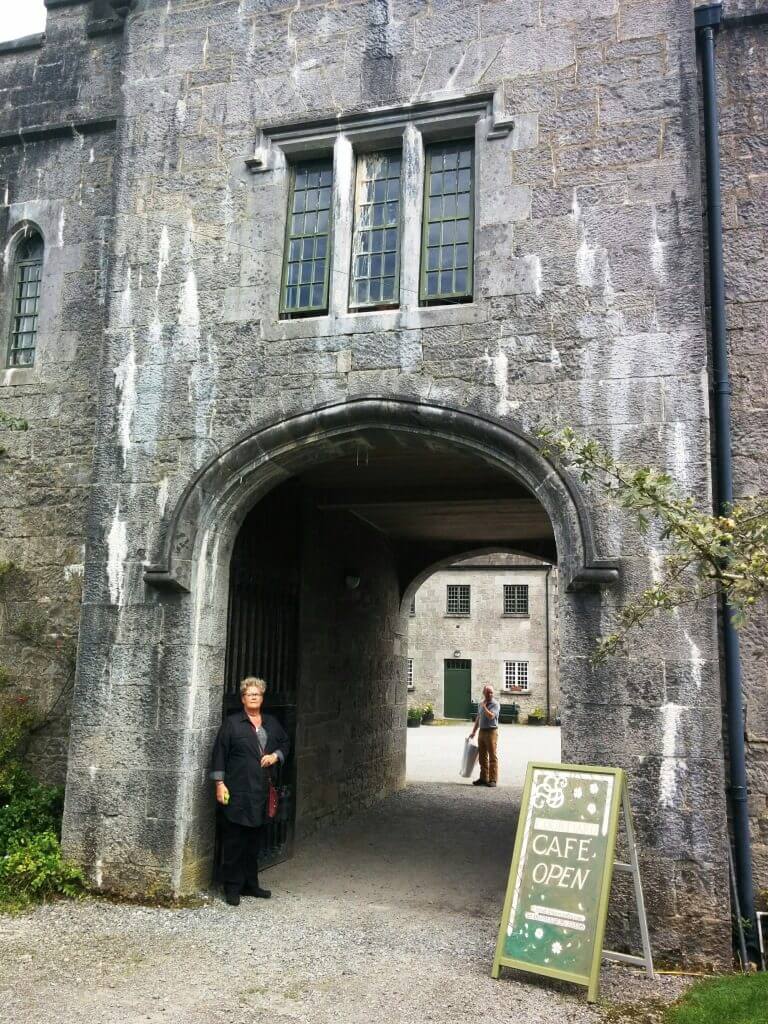 Woman stands near cafe open sign at stone archway entrance.