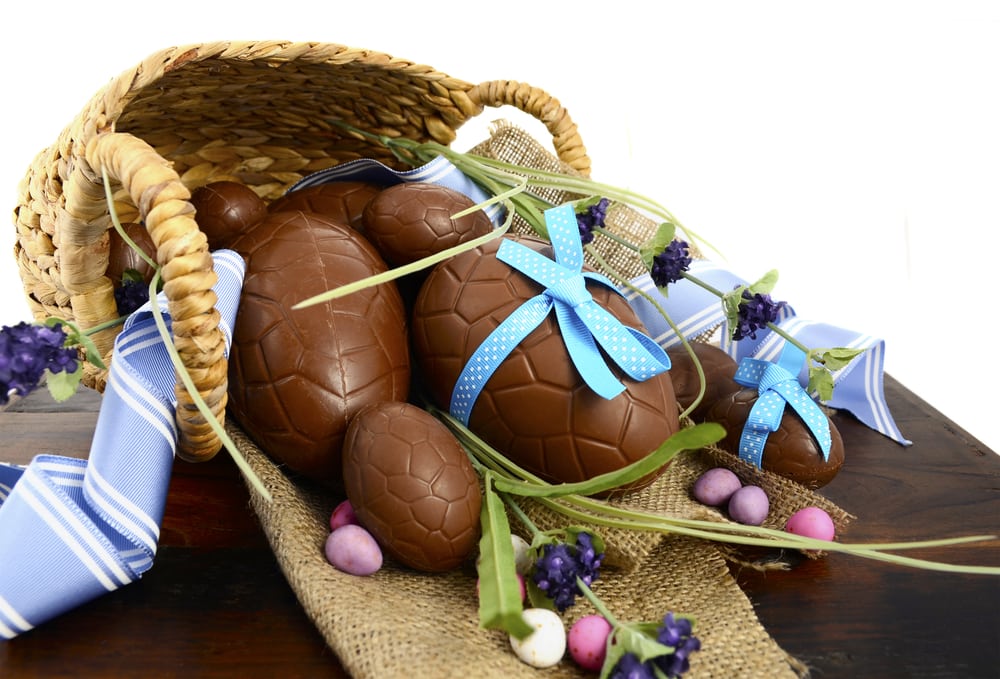 Happy Easter basket hamper of chocolate Easter Eggs and flower on dark wood table.