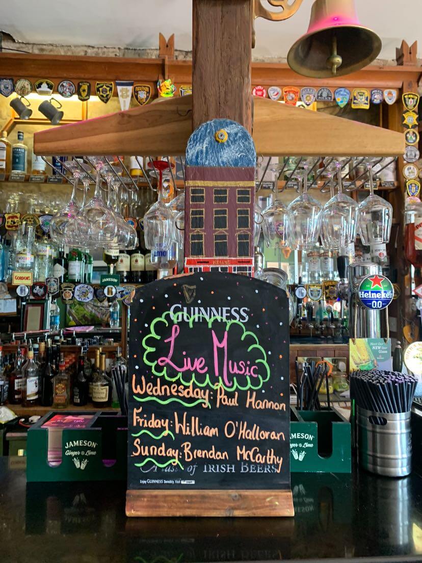 Guinness live music chalkboard sign on a bar with bottles and glasses.