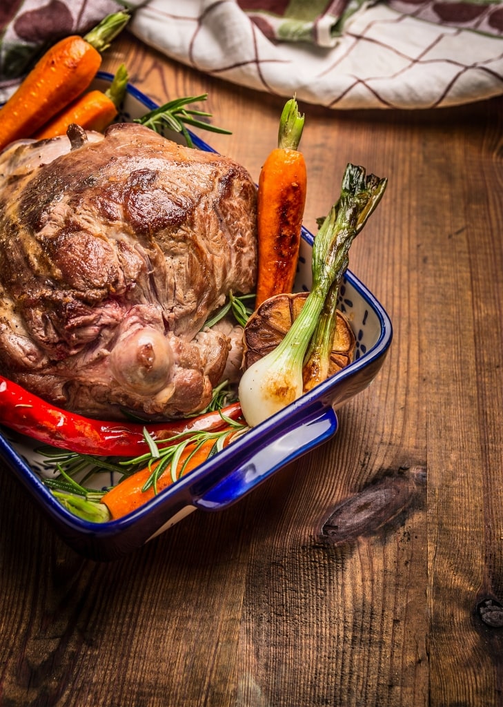 Roasted leg of lamb with herbs and vegetables on wooden background