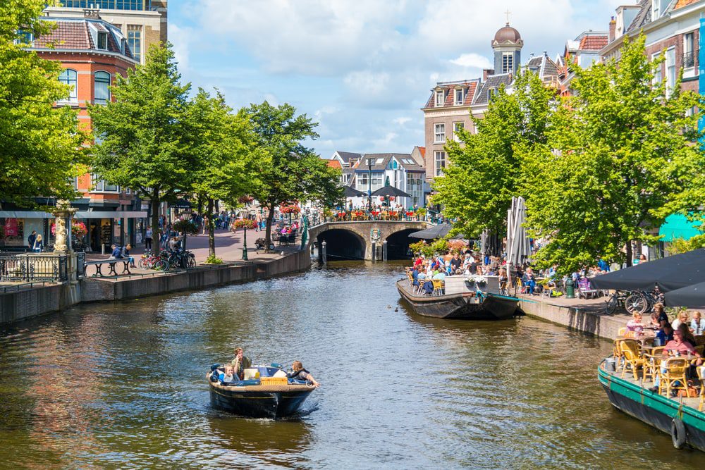 LEIDEN, NETHERLANDS - AUG 9, 2016: People in barge and outdoor terraces of cafes on New Rhine canal in old town of Leiden, South Holland, Netherlands