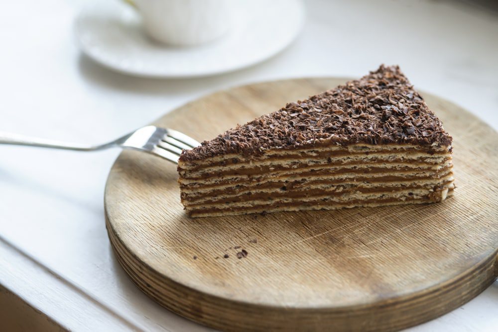 A slice of chocolate cake on a wooden plate, perfect for satisfying your cravings for decadent Armenian food.