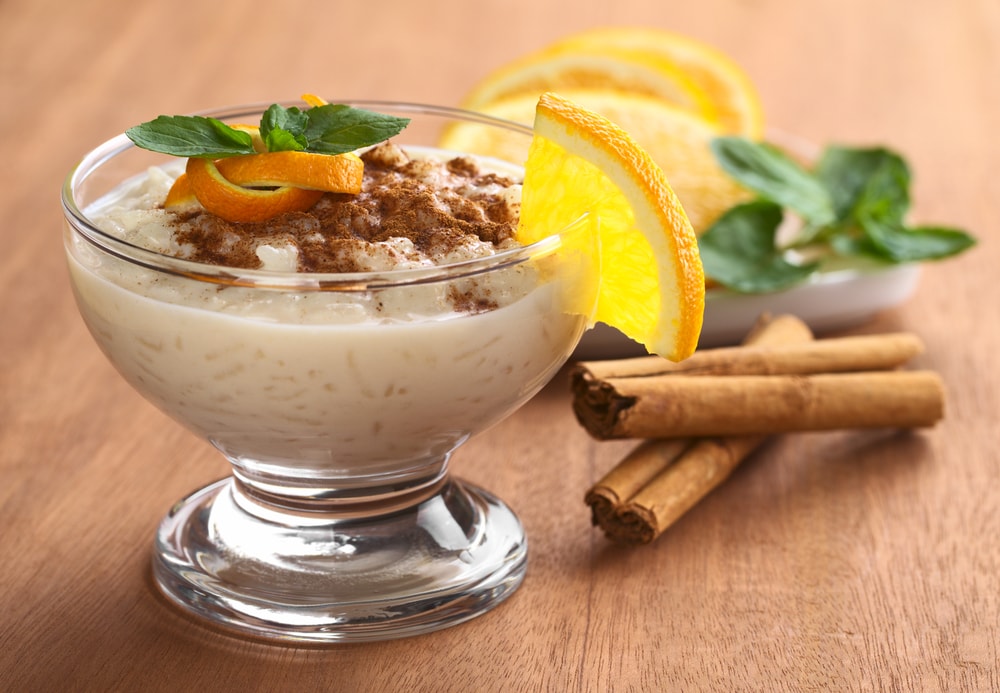 Delicious homemade rice pudding with cinnamon garnished with orange peel and mint leaf and a slice of orange on the rim of the bowl 