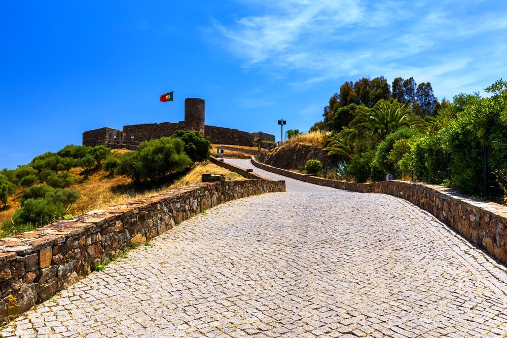 Ruins of Castle in Aljezur with waving Portuguese flag, Algarve, Portugal. Aljezur castle, Portugal Arabian gorgeous castle, made of stone with a tower. Aljezur, Algarve, Portugal.