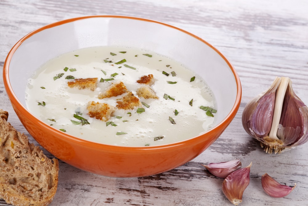 Garlic cream soup in orange bowl on white wooden background. Culinary healthy soup eating, rustic country style.