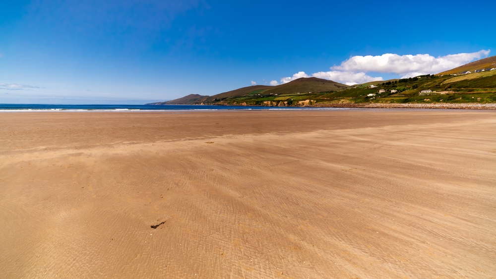 Long, beautiful sandy Inch Beach with mountains in background. Summer day with blue sky on empty beach, relaxation. Dingle peninsula, Ireland