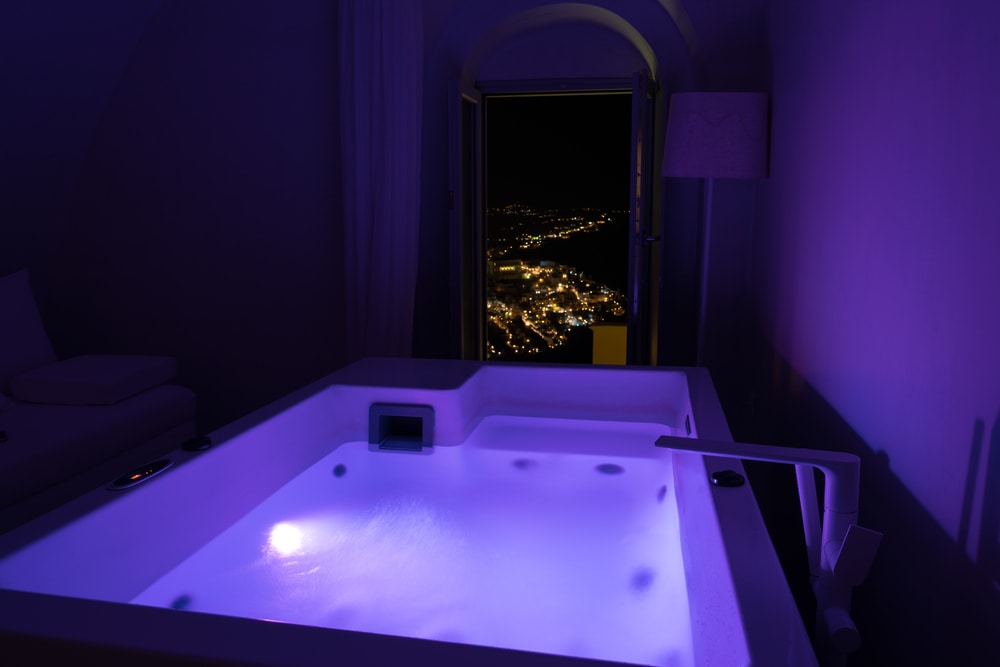 Luxury travel Santorini vacation hotel jacuzzi in colored lights with night view of the city. Europe resort destination holiday for honeymoon getaway.
