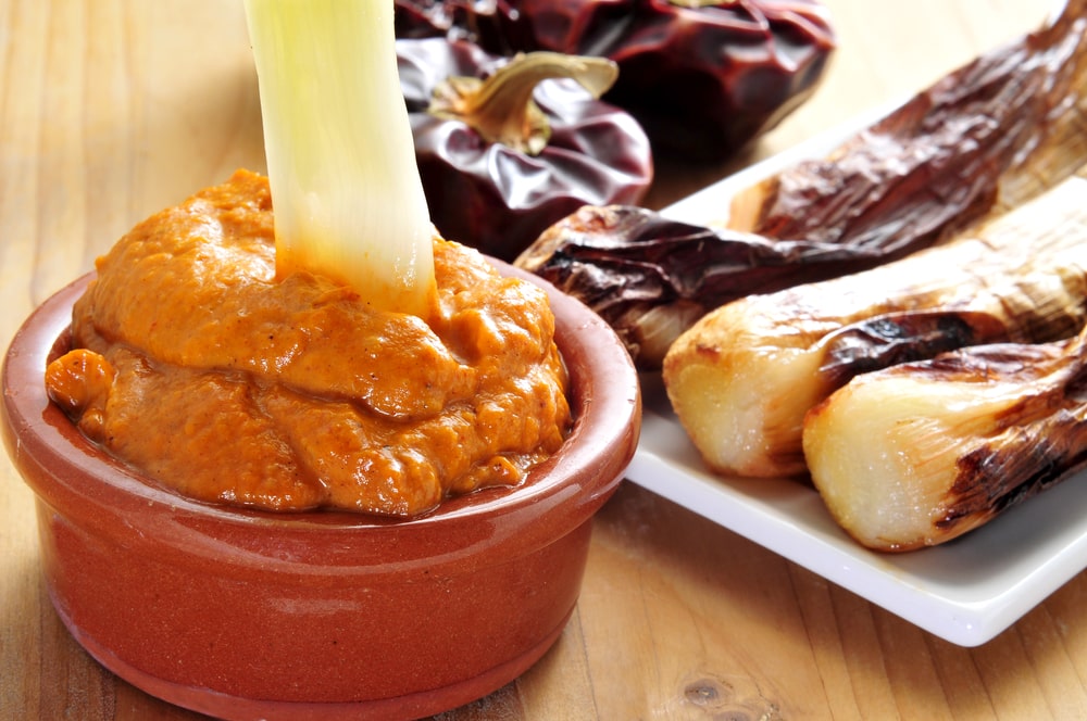 closeup of a plate with barbecued calcots, sweet onions, and a bowl with romesco sauce, typical of Catalonia, Spain