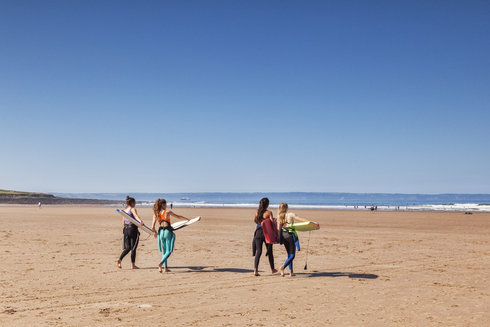 Croyde Bay, North Devon, England, UK - Four young women approach the sea with surfboards on one of the hottest days of the year.
