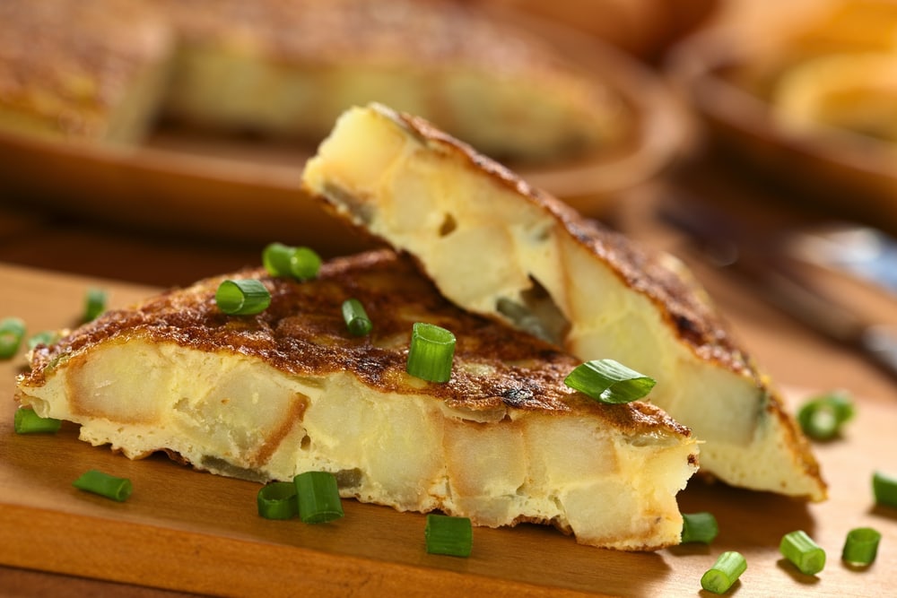 Fresh homemade Spanish tortilla (omelette with potatoes and onions) slices with scallion on top on wooden cutting board 