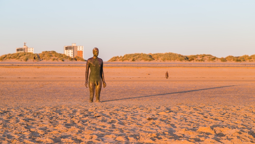 Long shadow behind an Iron Man at sunset on Crosby beach in April 2021.  This, and the one in the background are part of Another Place, the art installation near Liverpool made up of 100 Iron Men statues created by Antony Gormley.
