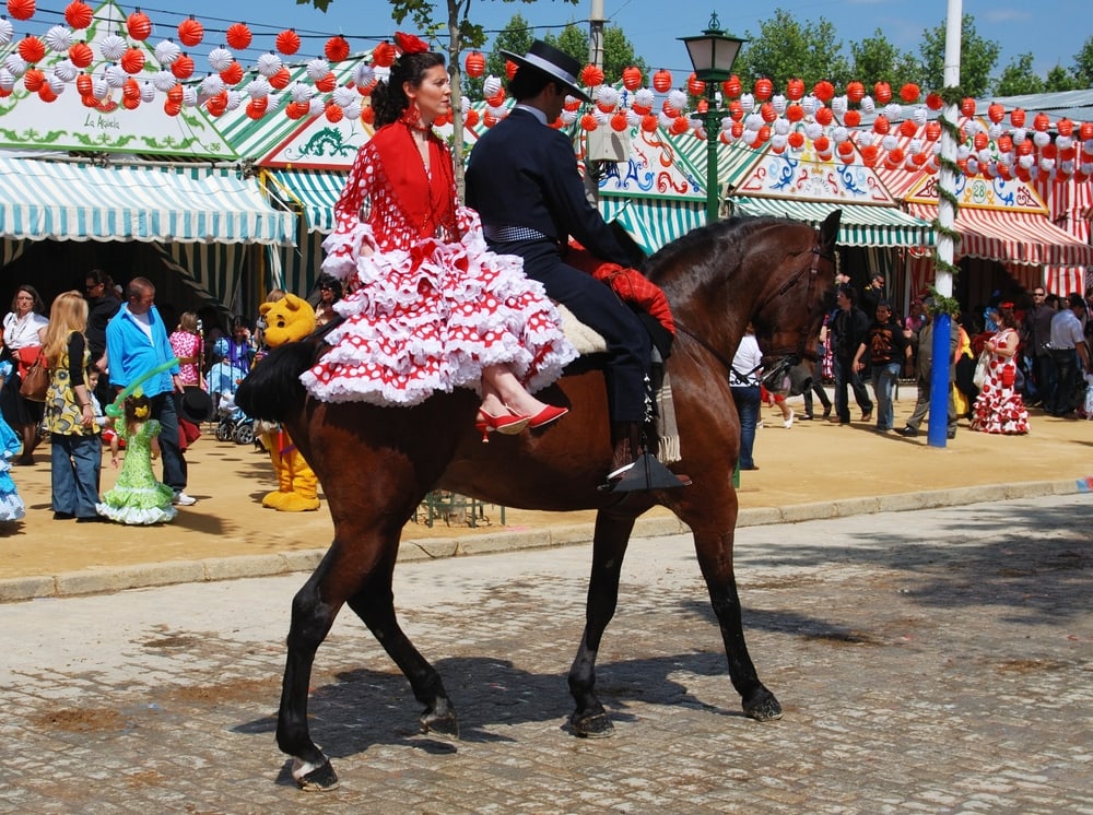Spanish couple in traditional dress sitting on a horse with Casitas to the rear at the Seville Fair, Seville, Seville Province, Andalusia, Spain, Western Europe.