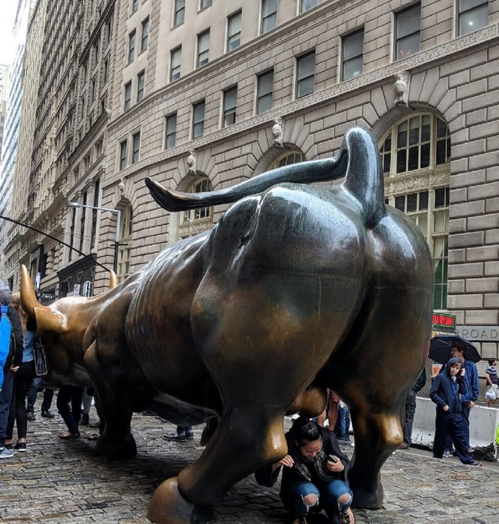 A bronze bull sculpture, one of the city's strangest art pieces, in a city setting with people around, some taking photographs.
