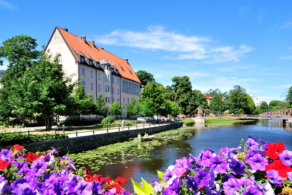 Very beautiful and cozy town in Sweden.  Uppsala. The house sits on the river bank with a bridge in the background and an array of colourful flowers in reds and purple