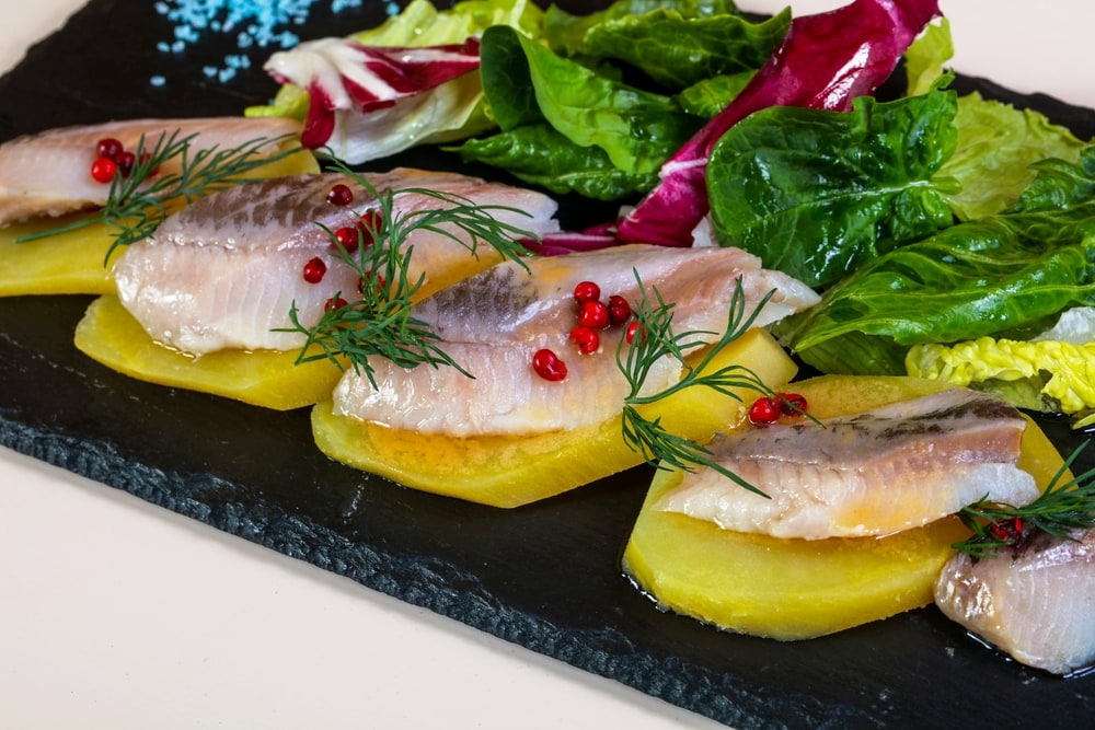 A slate platter of pickled herring on slices of potatoes topped with dill and pomegrante seeds