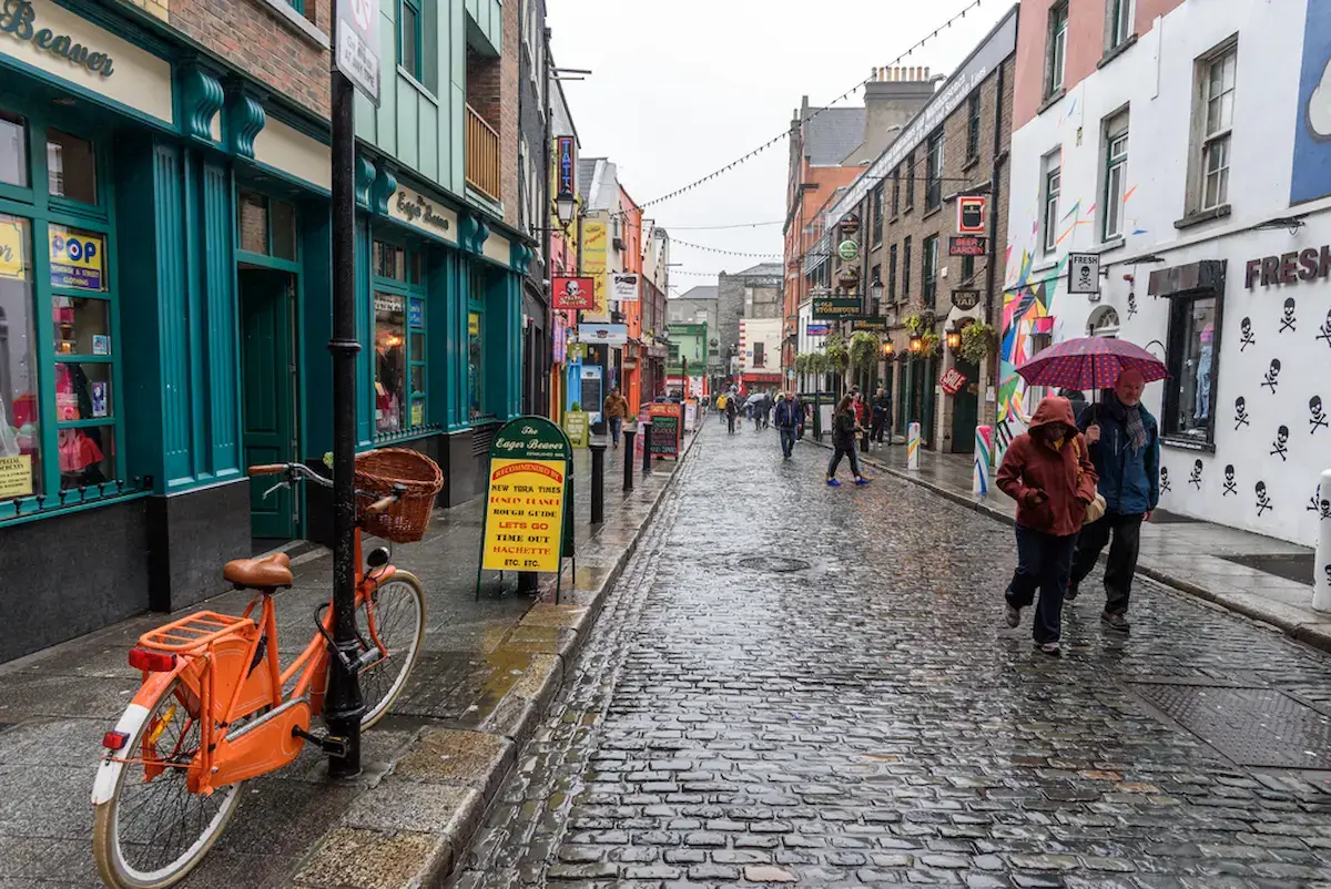 Cafes and bars on Crown alley in Dublin in the rain lots of folks walking with umbrellas