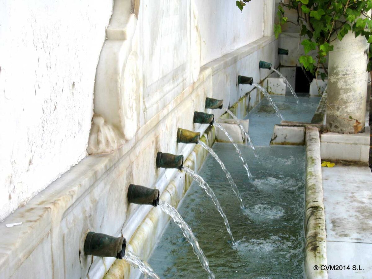 Water flows from a row of metal spouts into a long, narrow marble trough.