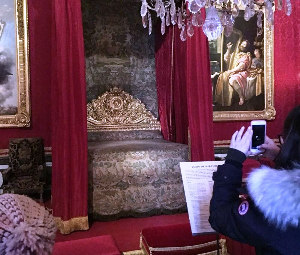 the Mercury Room, which was the royal bed chamber in the Palace of Versailles. It is festooned with burgundy drapery around a gold bed