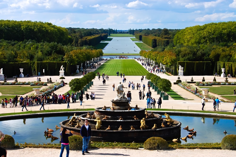 Versailles Castle gardens with fountain & tourists  background bright blue sky at Versailles in France 