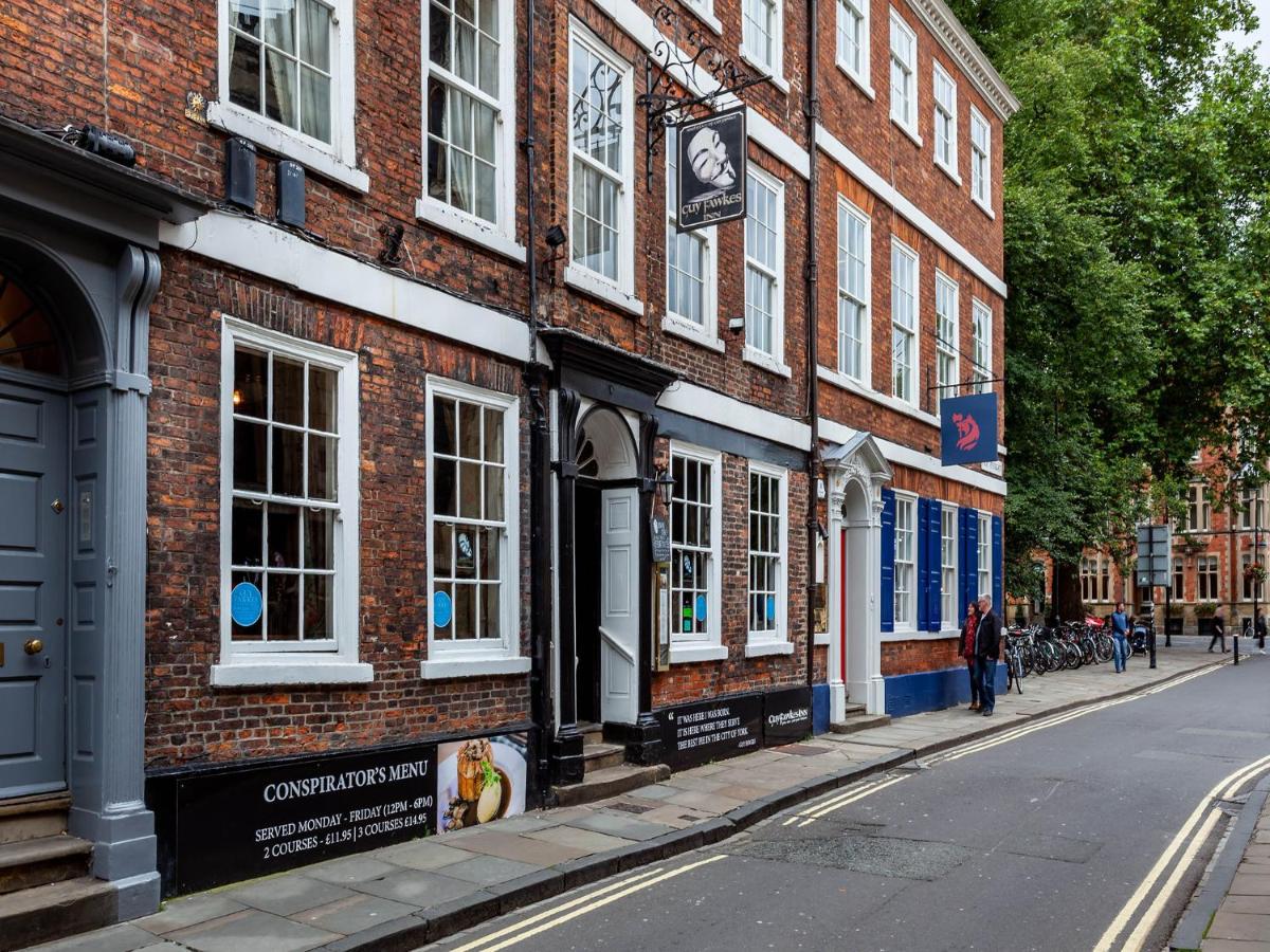 A brick building with a sign reading Guy Fawkes Inn stands along a street with people walking on the sidewalk.