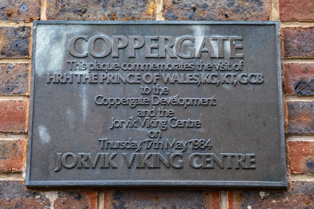 A metal plaque mounted on a brick wall commemorates a 1984 visit by the Prince of Wales to the Jorvik Viking Centre.