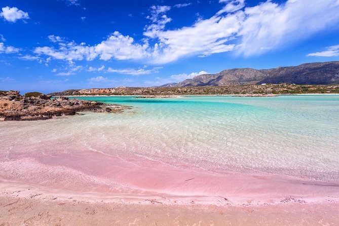 A pink sand beach with blue water and mountains in the background.