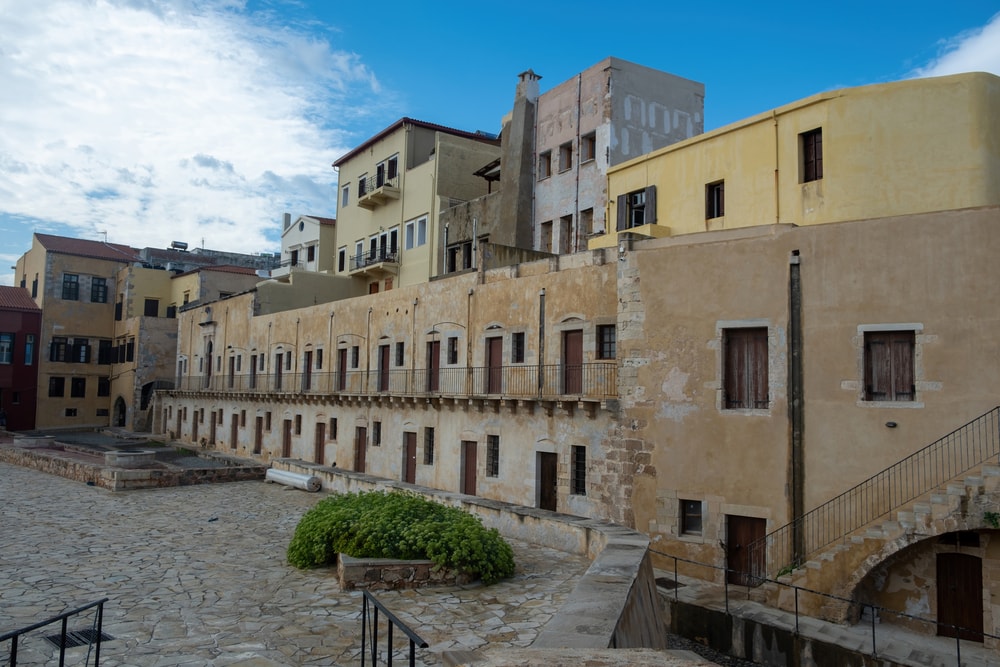 A group of buildings with a stone courtyard. War museum, Firkas Fortress at harbor of the Old Town of Chania Crete, Greece. Revellino castle, venetian fort, paved street, travel destination.