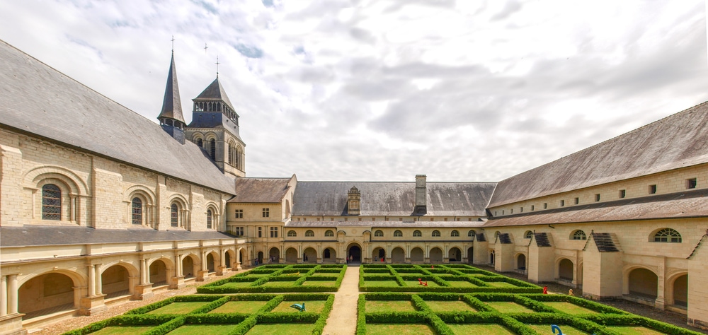 The Fontevraud Abbey courtyard, adorned with lush greenery, is situated within a magnificent large building.