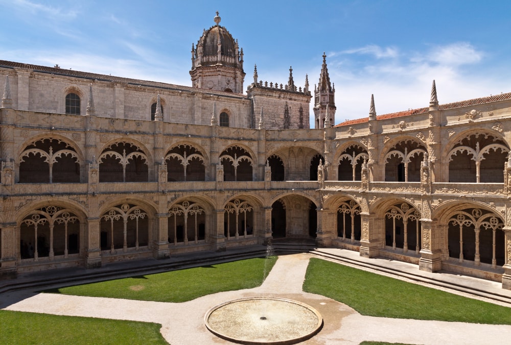 Jerónimos Monastery is not just any UNESCO World Heritage Site. Featuring elaborate sculptural details and towering pinnacles. A courtyard with arches and a fountain in the middle.
