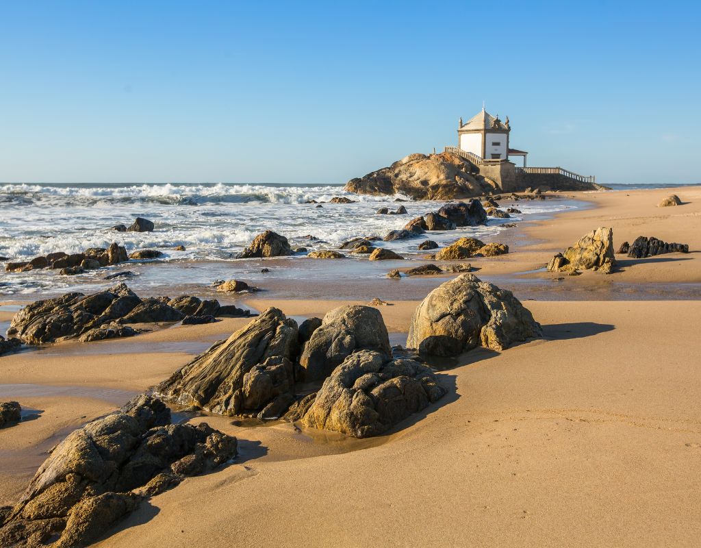 One of the best beaches in Portugal with rocks and a building.