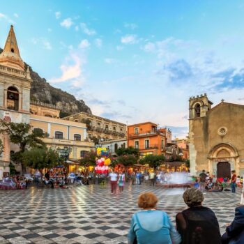 Set-jetting destinations Europe: People sitting on a square in front of historic buildings.