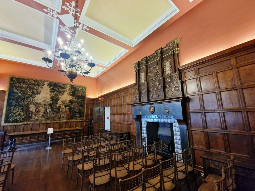 A large room with wooden paneling and a large tapestry, reminiscent of English manor houses.