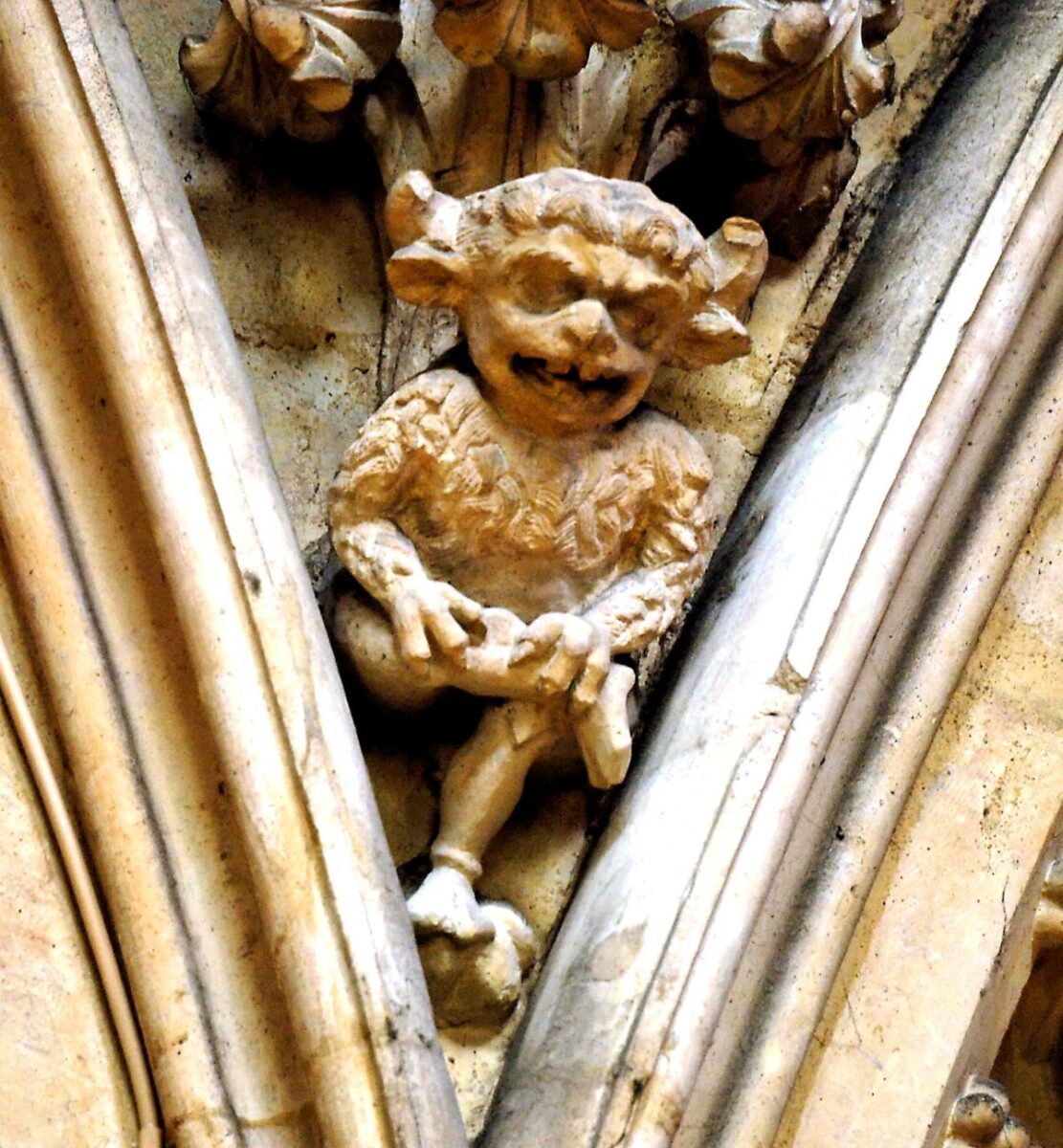 A stone carving of a horned, imp-like figure is nestled between two architectural arches.