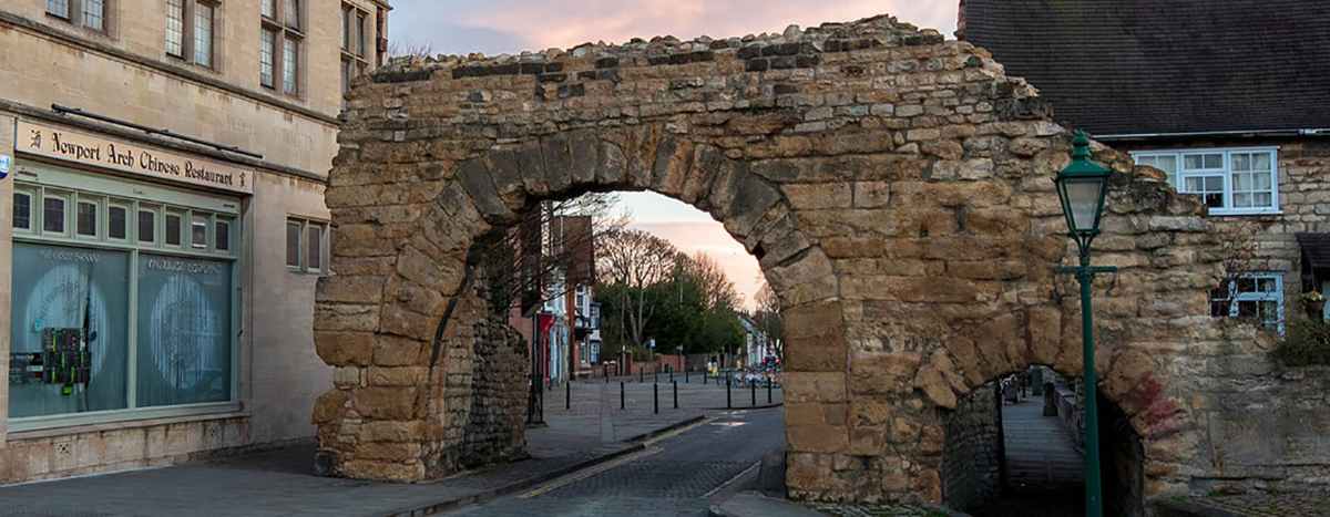 An ancient stone archway stands over a street next to a building with a sign for a Chinese restaurant.