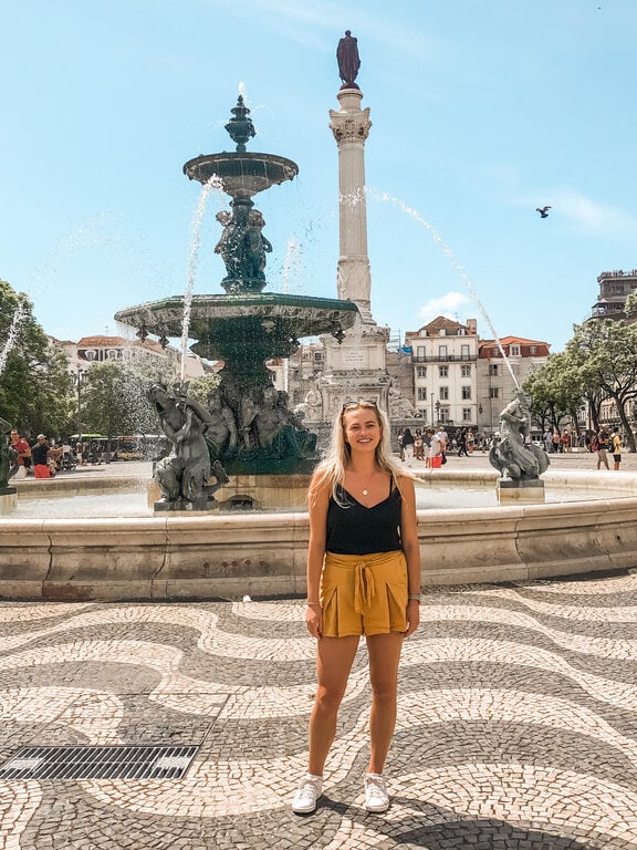 Officially known as Praça Dom Pedro IV, Rossio Square is another must-see site in Lisbon that holds a lot of history. It’s known as one of the city's most vibrant and historically significant public spaces located in the Baixa area. A woman standing in front of a fountain in lisbon.
