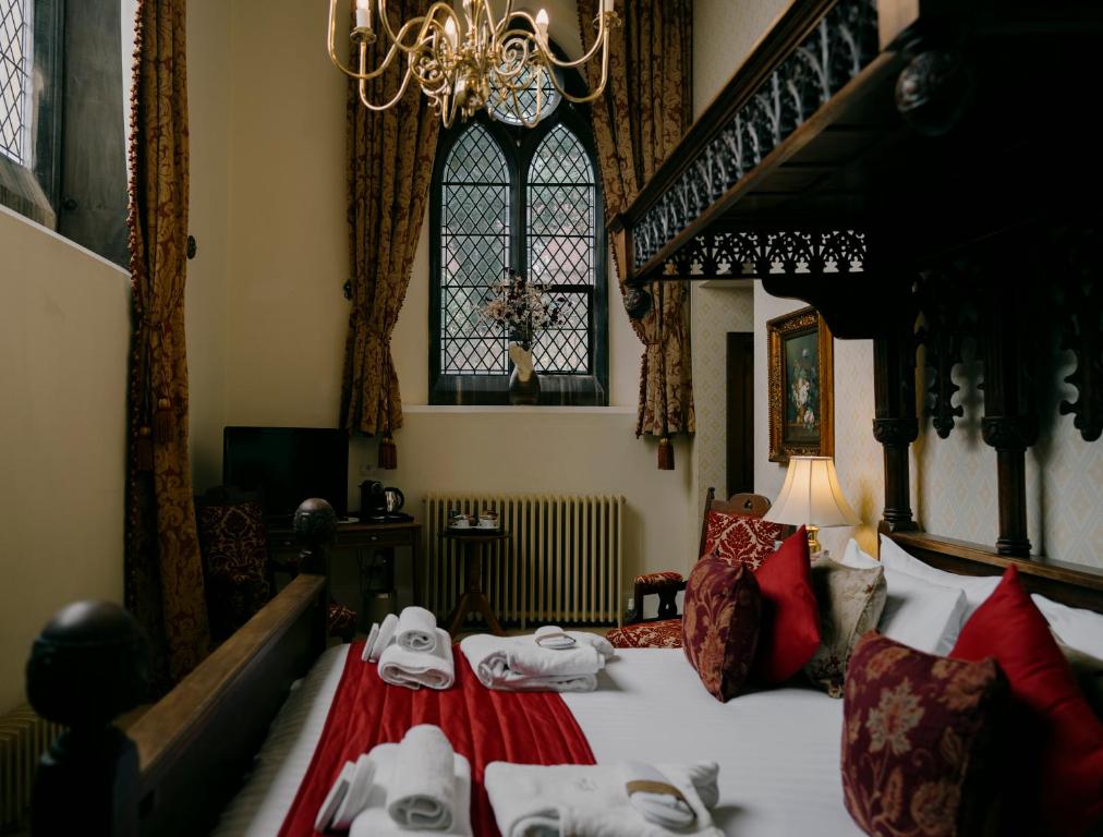 A bedroom features a four-poster bed with red accents, a chandelier, and a tall window with patterned curtains.
