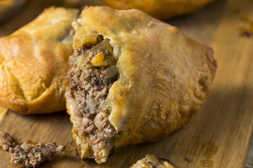 Hand pies with meat and cheese filling displayed on a rustic wooden cutting board. Homemade Upper MIchigan Pasty Meat Pie with Ketchup