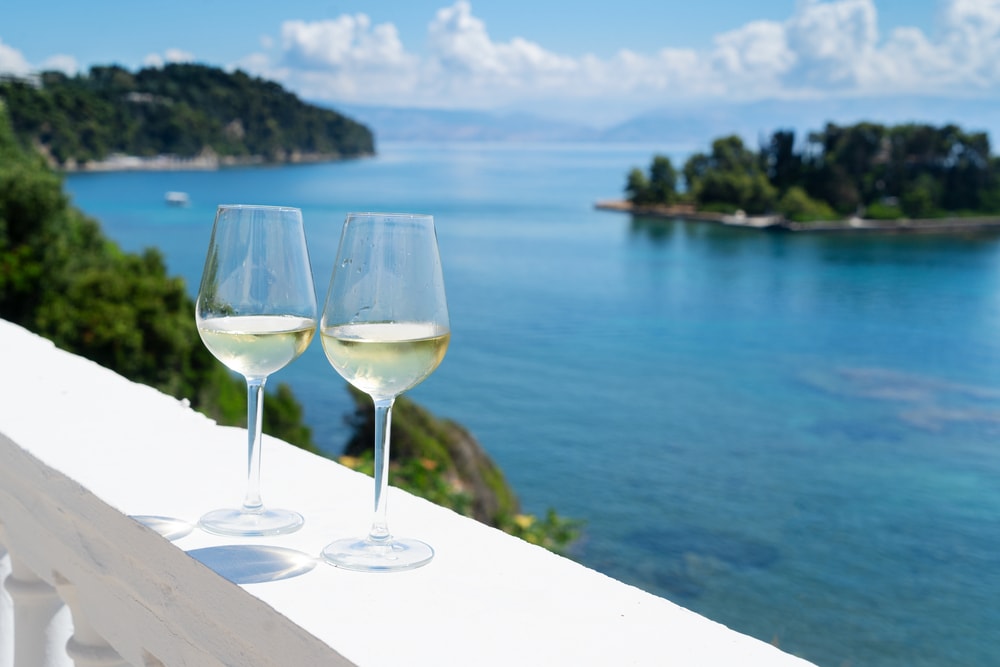 One of the best things to do in Corfu is sipping on two glasses of wine on a balcony with a view of a beautiful body of water.
