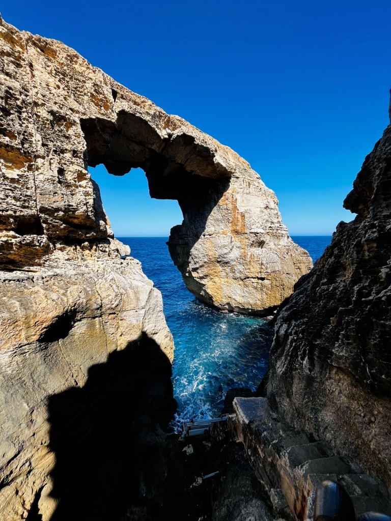 A natural stone arch over turquoise waters viewed from a rocky coastal perspective is one of the must-see things to do in Malta.