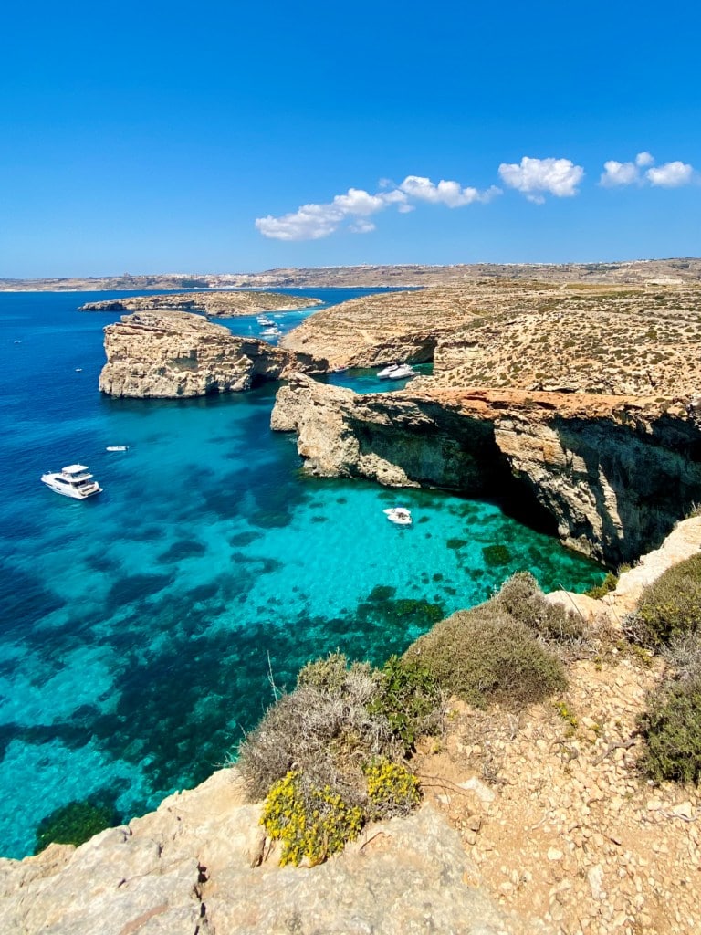 Crystal-clear turquoise waters along a rugged coastline with boats anchored near cliffs, offering an array of things to do in Malta.