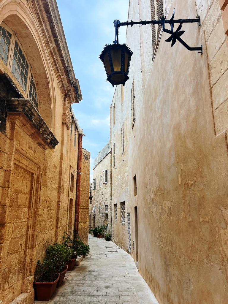 Narrow alleyway with stone buildings and a hanging lantern in an old european city.