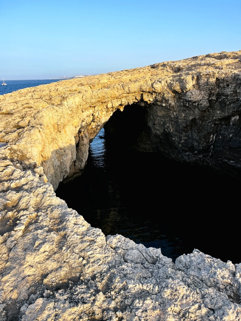 Rocky coastal arch formation over tranquil sea water with clear skies.