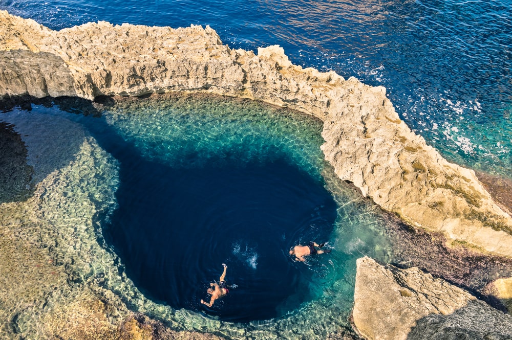 Deep blue hole at the world famous Azure Window in Gozo island - Mediterranean nature wonder in the beautiful Malta - Unrecognizable touristic scuba divers swimming to adventure water cave