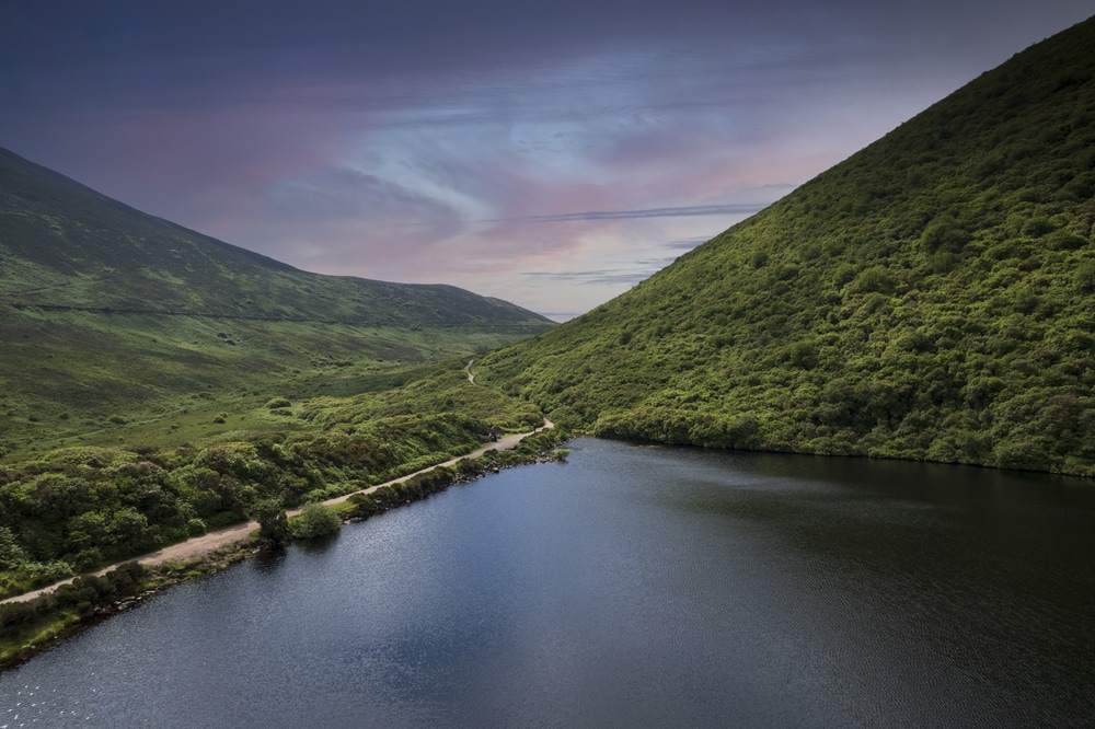 A serene landscape featuring a winding river nestled between lush green hills under a dusky sky, offering picturesque things to do in Tipperary. Bay Lough lake in Clogheen, county Tipperary in Ireland. The lake sits on a slope in the midst of the Knockmealdown mountains, looks like a mirror due to its black water.