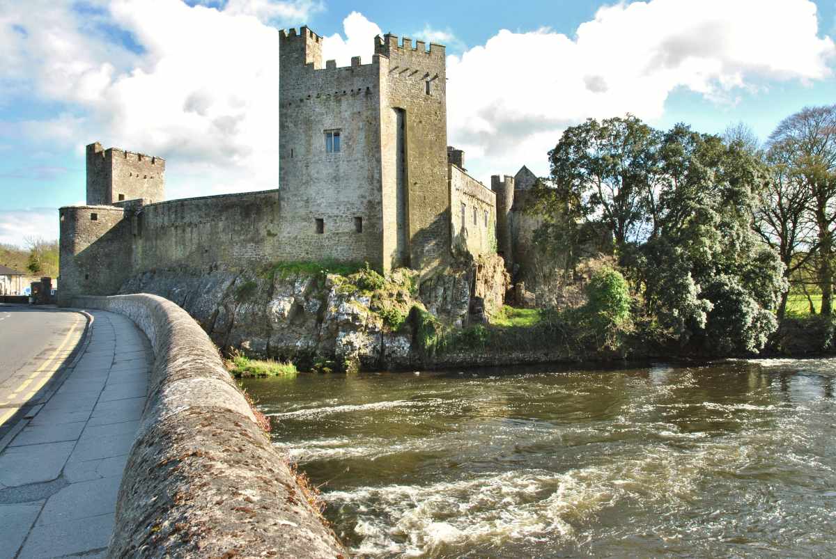Cahir Castle, a medieval fortress in Ireland, stands by the River Suir, viewed from a stone bridge.