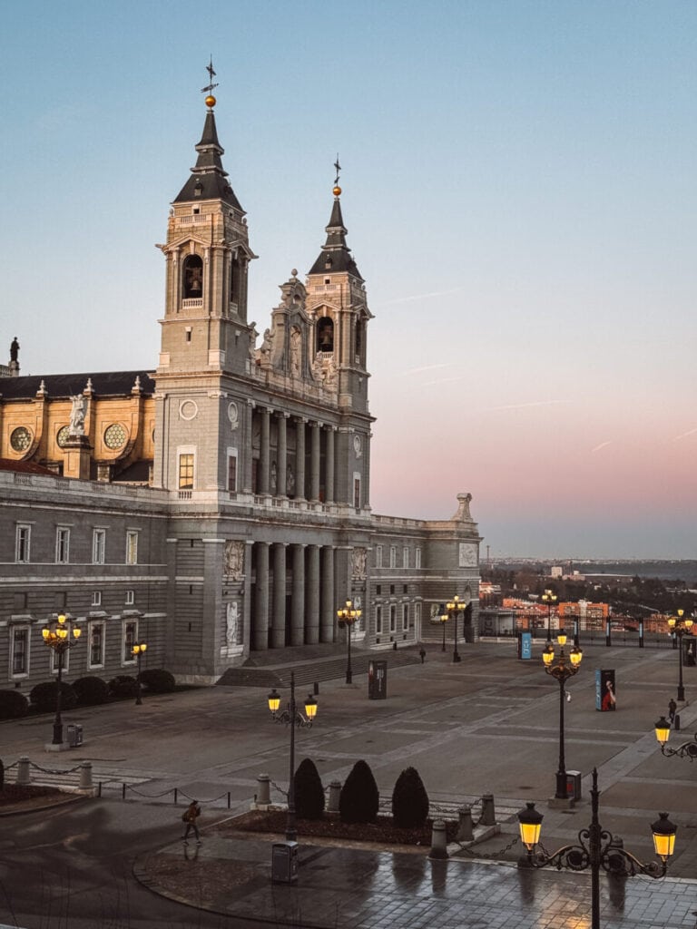Twilight view of a grand cathedral in Madrid with illuminated street lamps and a spacious square.