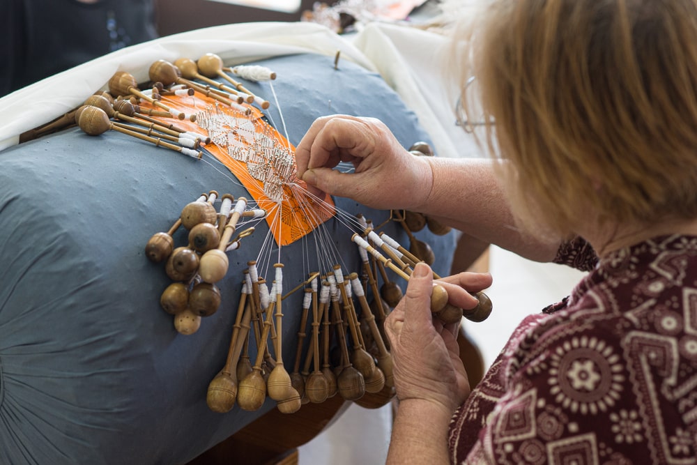 Croatian woman creates original lace with a cylinder for bobbin laces. Craftsperson creating intricate lace with bobbins on a pillow, showcasing one of the things to do in Split Croatia.