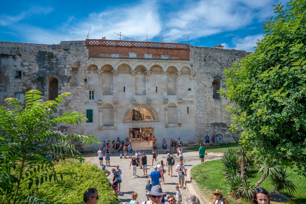 Golden Gate in Diocletian Palace in Split, Croatia. Tourists exploring the grounds in front of a historic stone building with archways on a sunny day, experiencing one of the top things to do in Split, Croatia.